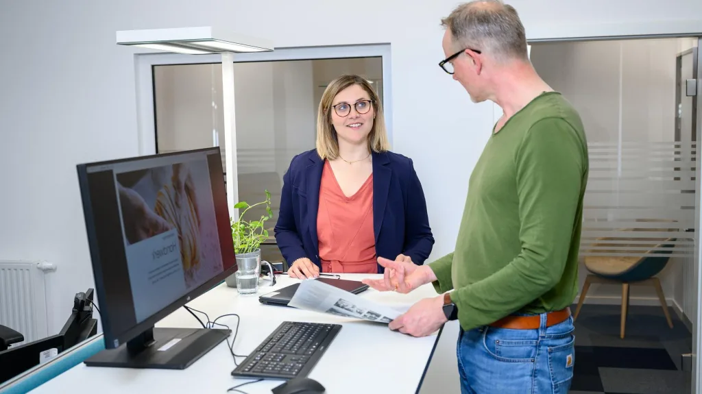 Alexander Gundlach spricht mit einem Kollegen an einem Schreibtisch mit Computer.