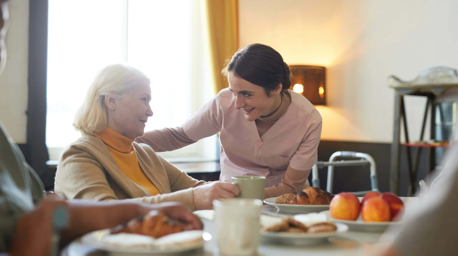 Eine Frau bedient eine Seniorin am Tisch.